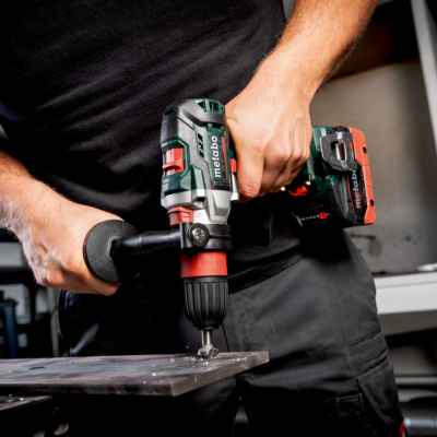 Pessoa a usar uma broca elétrica verde e preta para perfurar metal