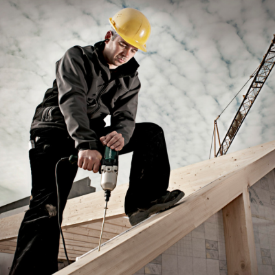 Trabalhador com capacete usa furadeira num telhado de madeira em construção