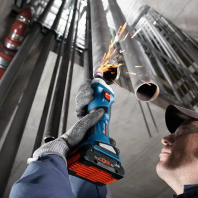 Homem a usar ferramenta elétrica para cortar tubo metálico num ambiente industrial