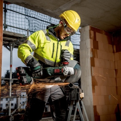 Trabalhador de construção civil com equipamento de segurança a usar rebarbadora Bosch em obra
