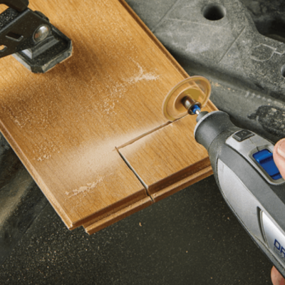 Ferramenta elétrica Dremel a cortar placa de madeira clara fixada em superfície de trabalho preta