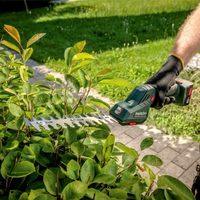 Aparelho aparador de sebe elétrico Metabo a cortar folhas verdes num jardim