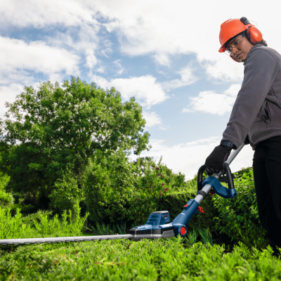 Pessoa a aparar sebes com aparador eléctrico num jardim verde