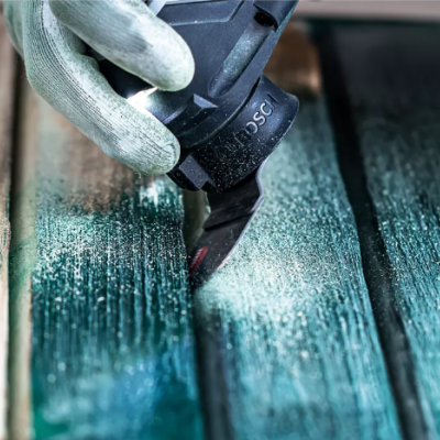 Mão com luva a pintar madeira com verniz verde-azulado usando ferramenta preta com texto 'BOSS'