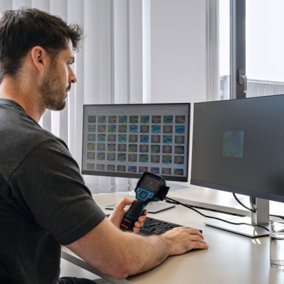 Homem com equipamento portátil à secretária frente a dois ecrãs de computador