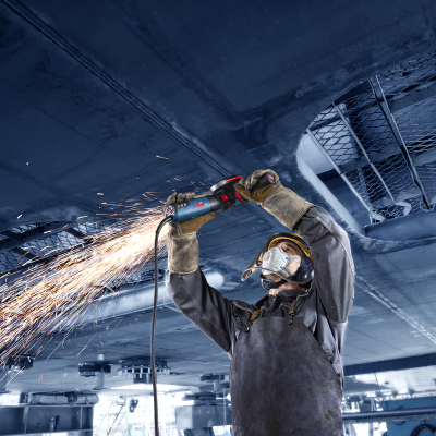 Trabalhador com equipamento de proteção a usar esmeril numa estrutura metálica azul