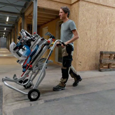 Homem transporta ferramenta elétrica num carrinho metálico num ambiente industrial.