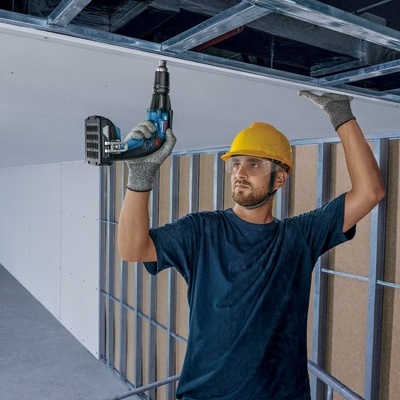 Trabalhador com capacete amarelo usando furadeira num teto em construção