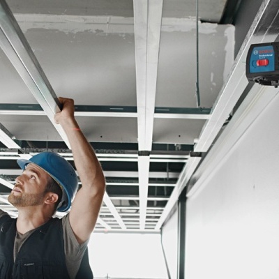 Homem a trabalhar numa estrutura metálica de teto suspenso com equipamento laser Bosch fixado na parede