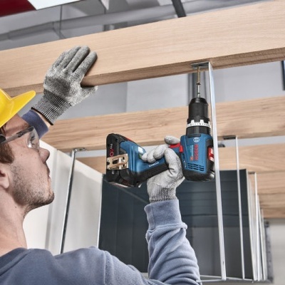 Homem com capacete a usar parafusadeira elétrica para fixar madeira no teto