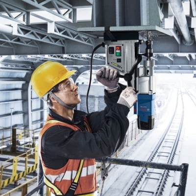 Trabalhador com capacete e colete usando máquina perfuradora em estação ferroviária