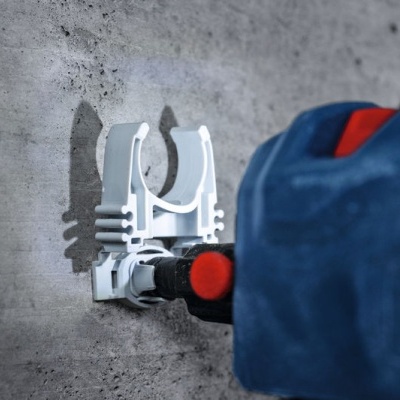 Ferramenta branca presa a uma parede de cimento cinza com uma mão de luva azul segurando-a