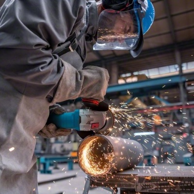 Homem a usar rebarbadora em tubo metálico com faíscas, em ambiente industrial