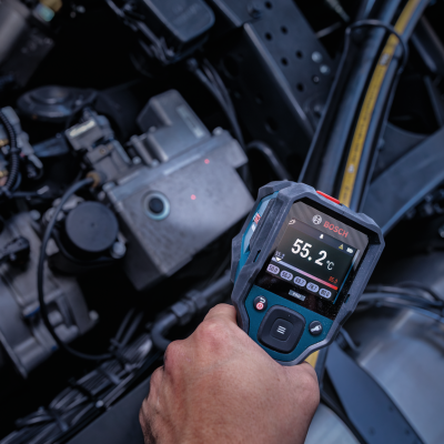 Medidor de temperatura BOSCH com tela digital nas mãos diante de motor automóvel