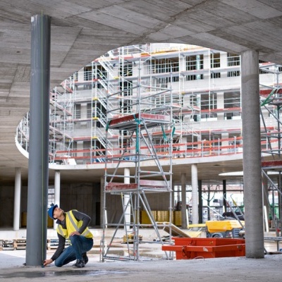 Área de construção com andaimes e trabalhador perto de pilar de concreto