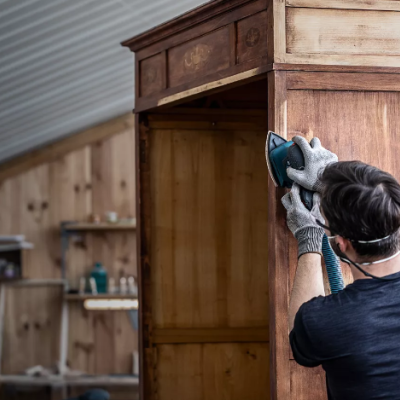 Homem a lixar móvel de madeira antiga numa oficina