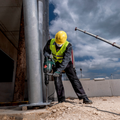 Trabalhador com capacete e colete a usar ferramenta elétrica numa obra ao ar livre