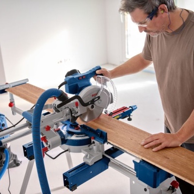 Homem a usar serra de esquadria azul a cortar madeira numa sala clara