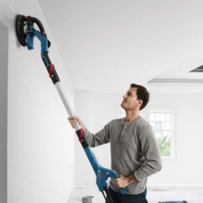 Homem a usar lixadora elétrica de pega longa para parede branca