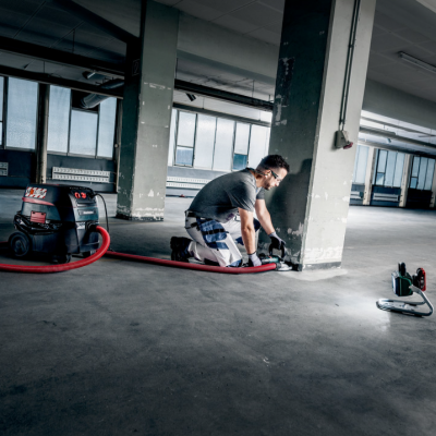 Homem a trabalhar com máquina industrial num espaço com chão de cimento e colunas