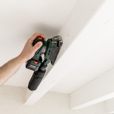 Ferramenta elétrica verde e preta usada em estrutura de madeira branca no teto.