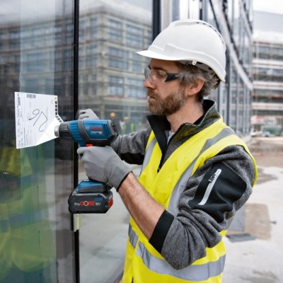 Homem com capacete a aplicar papel em vidro com furadeira