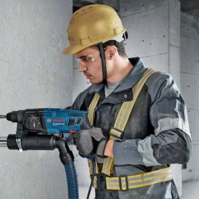 Homem com capacete e roupa de construção usando ferramenta elétrica numa parede
