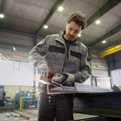 Homem a usar lixadora elétrica em peça metálica numa oficina industrial
