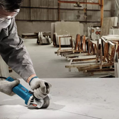 Trabalhador a usar esmerilhadora azul em superfície de mármore numa fábrica