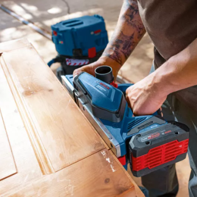 Pessoa a usar plaina elétrica portátil sobre porta de madeira clara num ambiente de oficina