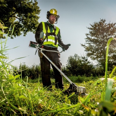 Homem a cortar ervas com desbastadora num campo verde.
