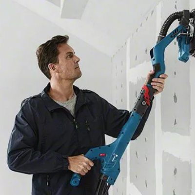 Homem usando lixadeira elétrica azul para lixar parede branca