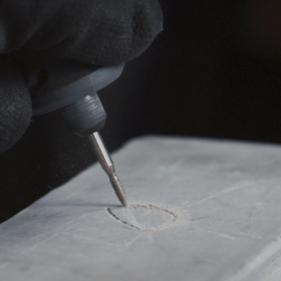 Mão com luva preta usando ferramenta elétrica de precisão numa superfície cinza clara