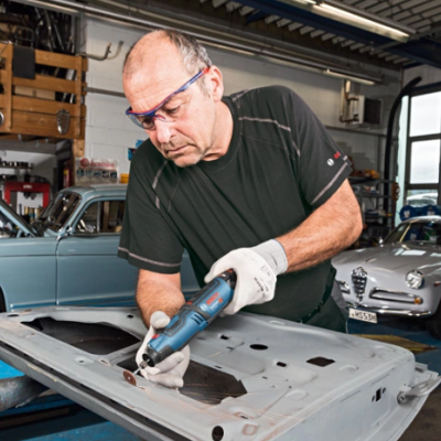 Homem a trabalhar numa porta de automóvel em oficina com carros clássicos