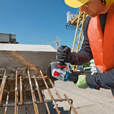 Homem com colete laranja e capacete amarelo cortando barras de ferro numa construção