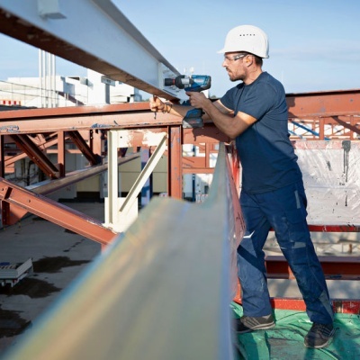 Trabalhador com capacete e ferramenta elétrica em obra com estruturas metálicas