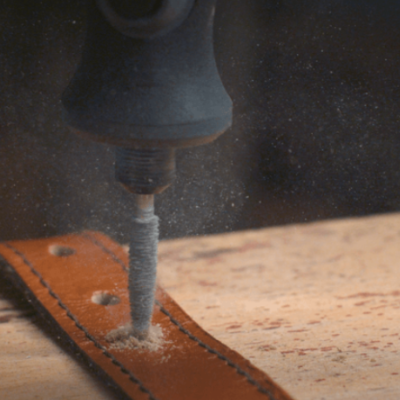 Broca elétrica a perfurar couro castanho numa superfície de madeira clara