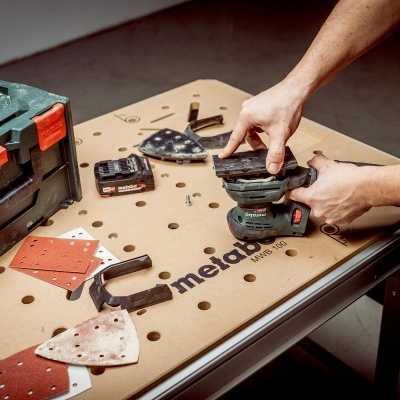 Mesa de trabalho com caixa de ferramentas e lixadora Metabo em uso
