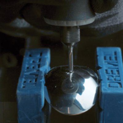 Esfera metálica sendo trabalhada segurada por peças azuis com texto 'DRAPER'