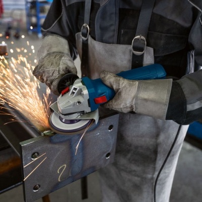 Trabalhador com rebarbadora a polir uma chapa de metal em ambiente industrial