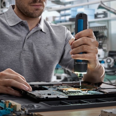 Homem a reparar computador portátil com chave de parafusos elétrica na oficina