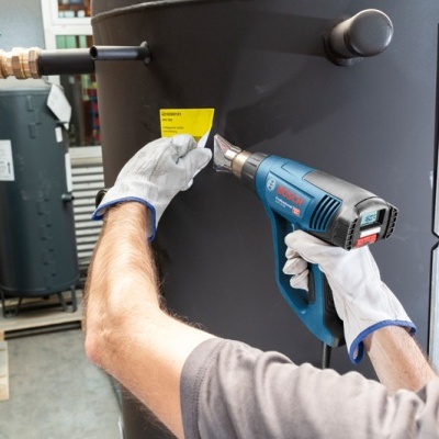 Homem usando pistola de calor para aplicar adesivo amarelo em equipamento industrial preto