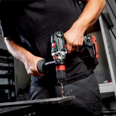 Pessoa a usar furadeira sem fios preta com detalhes vermelhos para perfurar chapa metálica