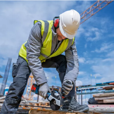Trabalhador da construção com colete amarelo e capacete branco usando esmerilhadeira em obra