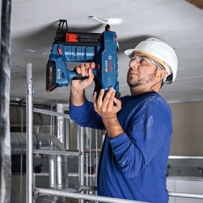 Trabalhador com ferramenta elétrica a furar teto em obra