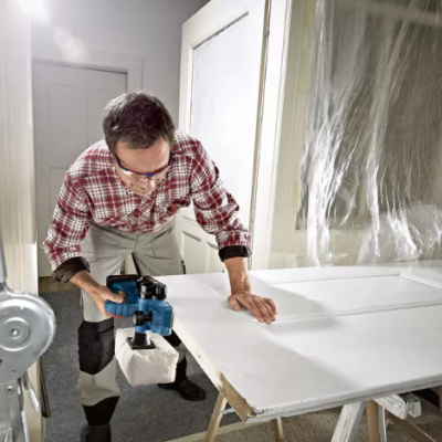 Homem a cortar uma porta branca com aparelho eléctrico numa bancada de trabalho