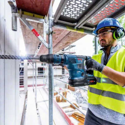 Homem a usar furadeira azul para perfurar parede branca em canteiro de obras