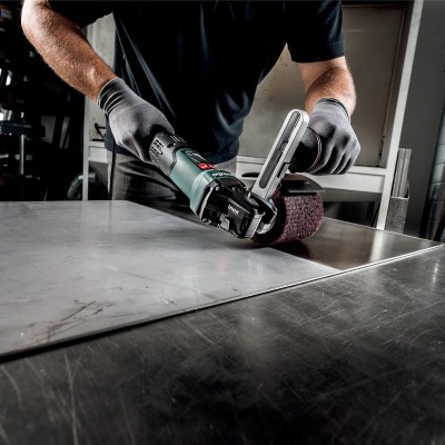 Pessoa a usar lixadora elétrica preta e verde numa oficina