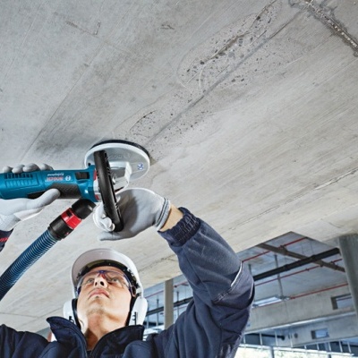 Pessoa a usar lixadora elétrica azul num teto de betão