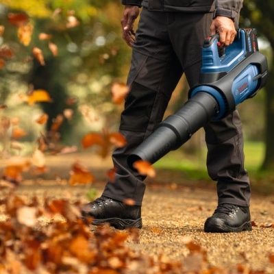 Soprador de folhas azul e preto em uso num parque com folhas secas a voar.